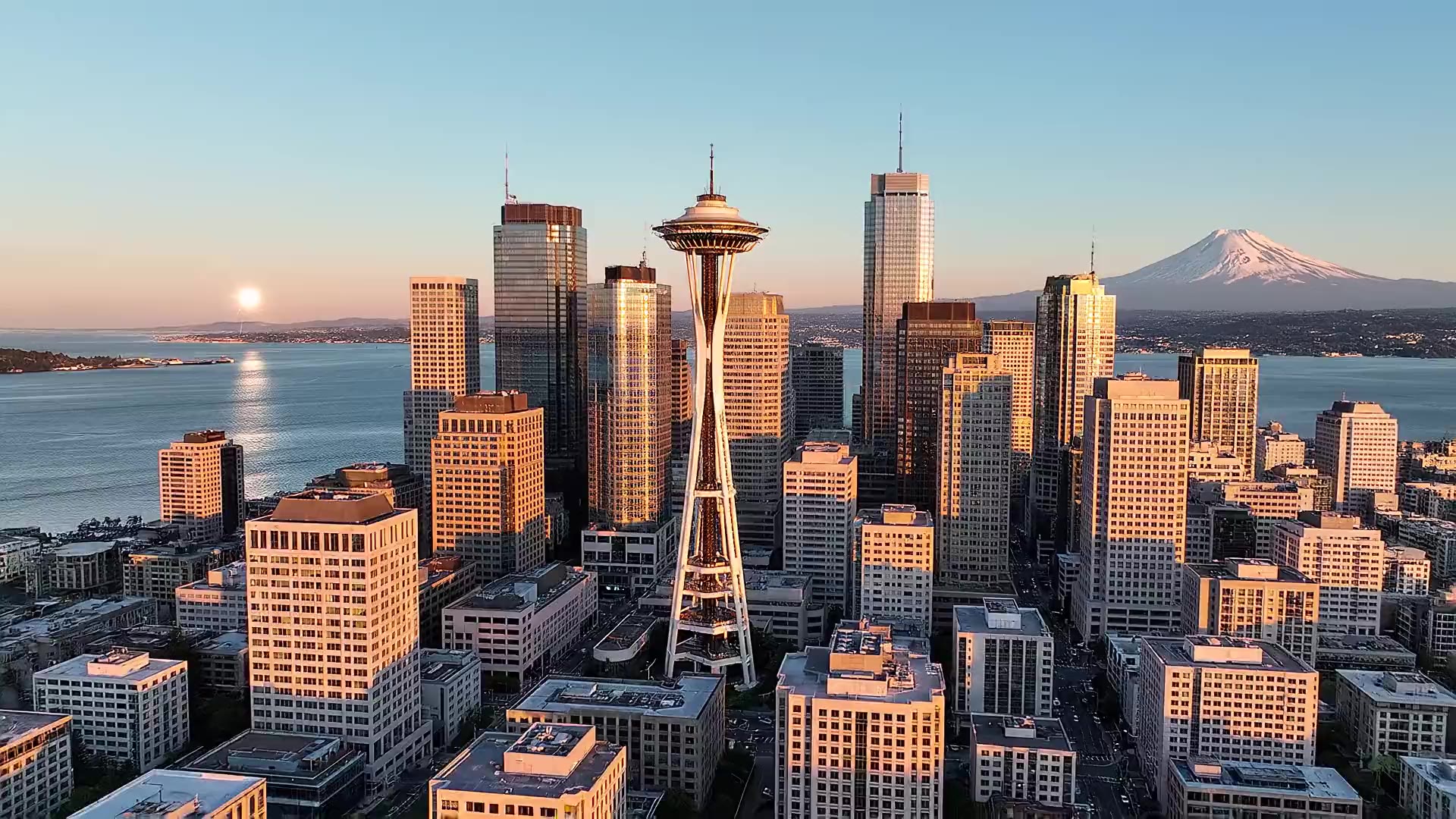Aerial view of the downtown Seattle skyline at golden hour with the Space Needle, Elliott Bay and Mount Rainier. Illustrative AI-generated concept footage.